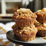 Close-up view of a moist Pear Cardamom Oatmeal Muffin, highlighting its golden-brown top and chunks of pear.