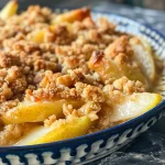 A close-up side view of a warm pear crumble, showcasing the golden-brown topping and sliced pears.