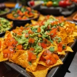 Close-up view of a mini pumpkin overflowing with nacho cheese and served with tortilla chips.