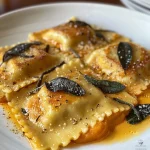 Close-up view of pumpkin ravioli drizzled with brown butter sauce and topped with sage leaves.