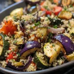 A close-up view of a bowl filled with quinoa and colorful roasted Mediterranean vegetables.