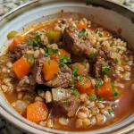 Close-up view of a hearty bowl of beef barley soup with visible chunks of beef and vegetables.