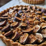 Close-up side view of a Spiced Fig and Walnut Tart with a golden crust and garnished with orange zest.