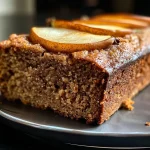 A close-up side view of a sliced spiced pear bread showing juicy pear chunks and a golden crust.