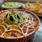 Close-up view of a creamy spiderweb dip with layers of refried beans, guacamole, and sour cream.