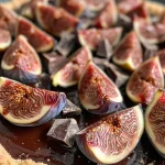 Close-up view of a vegan chocolate fig tart with a glossy chocolate filling and sliced figs on top.
